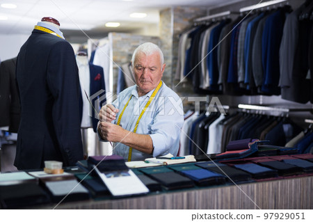 Mature tailor makes measurements of business suit at studio 97929051