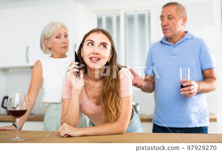 Elderly parents eavesdrop on the phone conversation of their adult daughter in kitchen 97929270