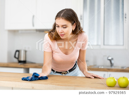 Focused woman wearing casual clothes cleaning countertop in kitchen with rag and detergent 97929365