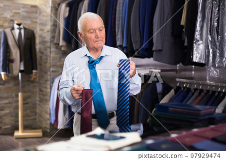 Mature senior citizen chooses fashionable tie in clothing store 97929474