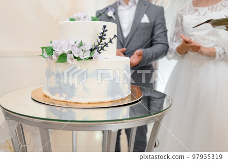 The bride and groom are standing next to their celebration cake. The bride and groom are standing next to their celebration cake. 97935319