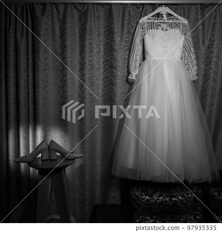 The wedding dress hangs on the cornice, a beam of colored light is directed at the dress. 97935335