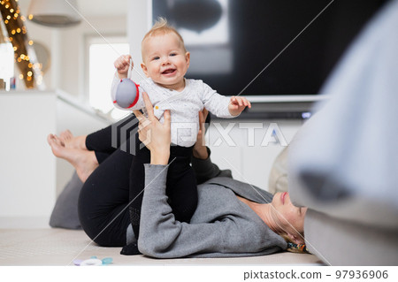 Happy family moments. Mother lying comfortably on children's mat playing with her baby boy watching and suppervising his first steps. Positive human emotions, feelings, joy 97936906