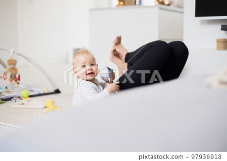 Happy family moments. Mother lying comfortably on children's mat playing with her baby boy watching and suppervising his first steps. Positive human emotions, feelings, joy Happy family moments. Mother lying comfortably on children's mat playing with her baby boy watching and suppervising his first steps. Positive human emotions, feelings, joy 97936918