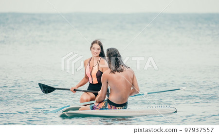 Sea woman and man on sup. Silhouette of happy young woman and man, surfing on SUP board, confident paddling through water surface. Idyllic sunset. Active lifestyle at sea or river. Sea woman and man on sup. Silhouette of happy young woman and man, surfing on SUP board, confident paddling through water surface. Idyllic sunset. Active lifestyle at sea or river. 97937557