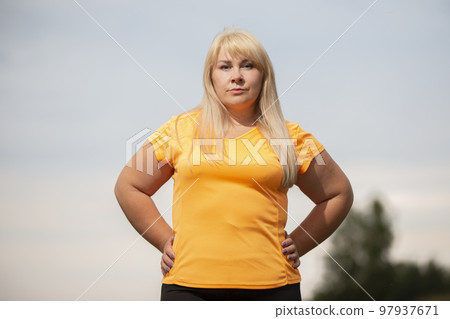 Portrait of a European middle-aged woman in a tracksuit, posing for the camera, relaxing. excited overweight woman in trendy tracksuit resting after exercising. 97937671