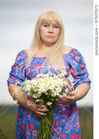 Beautiful plus size woman with white hair in a summer dress posing outdoors with daisies. Chubby girl in a meadow with flowers. Beautiful plus size woman with white hair in a summer dress posing outdoors with daisies. Chubby girl in a meadow with flowers. 97937672