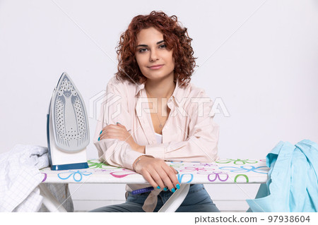 The girl sits at the ironing board with a gentle smile. The girl sits at the ironing board with a gentle smile. 97938604