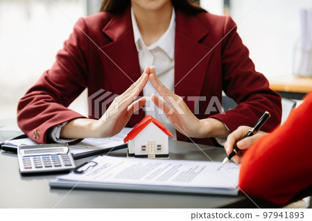 Female real estate agent is use hands to protect red roof for the concept of real estate investment about house trading, purchase at desk in office . 97941893