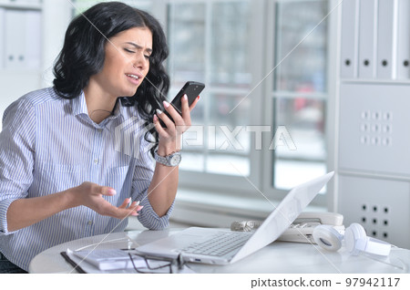 Beautiful young woman with phone working in office Beautiful young woman with phone working in office 97942117
