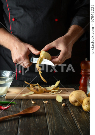 Chef peels raw potatoes in a hotel kitchen before preparing a national dish. Close-up of a cook hands with a knife while working Chef peels raw potatoes in a hotel kitchen before preparing a national dish. Close-up of a cook hands with a knife while working 97942223