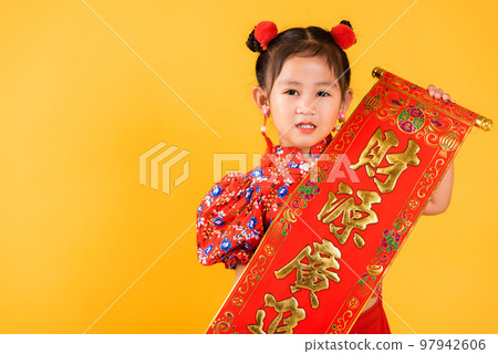 Chinese New Year. Happy Asian Chinese little child girl smile wearing red cheongsam qipao Spring festival couplets (Character FU means fortune, blessing), studio short isolated on yellow background 97942606