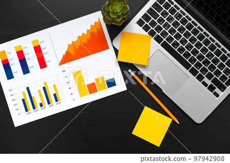Printed graphs and laptop on dark gray surface Printed graphs and laptop on dark gray surface 97942908