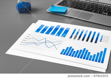 Printed graphs and laptop on dark gray surface Printed graphs and laptop on dark gray surface 97942935