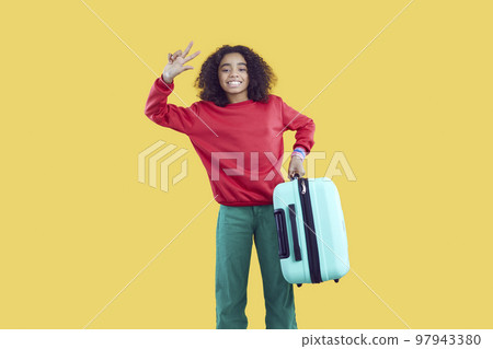 Happy cute african american teenage girl holding travel suitcase isolated on yellow background. Happy cute african american teenage girl holding travel suitcase isolated on yellow background. 97943380