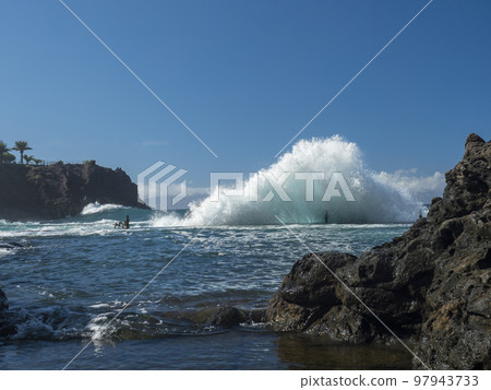 View of natural rock swimming pool Charco de Isla Cangrejo in the Atlantic Ocean in Los Gigantes, Tenerife, Canary islands, Spain. Sunny winter day. View of natural rock swimming pool Charco de Isla Cangrejo in the Atlantic Ocean in Los Gigantes, Tenerife, Canary islands, Spain. Sunny winter day. 97943733
