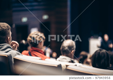 Speaker giving a talk in conference hall at business event. Rear view of unrecognizable people in audience at the conference hall. Business and entrepreneurship concept 97943958