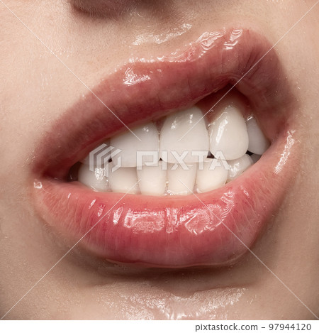Anger. Close-up expressive female mouth with white straight teeth grimacing. Sensual woman's lips covered gel. Beauty, makeup, sensuality concept 97944120