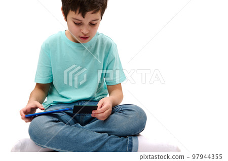 Close-up teenage boy holding credit card and smartphone, buying via internet, isolated over white background. Copy advertising space. Online payment. Money transfer. Internet banking. Transaction 97944355