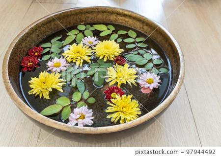 Pretty floating daisy flower petals and leaves on water in container as decoration Pretty floating daisy flower petals and leaves on water in container as decoration 97944492