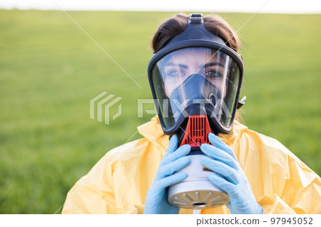 Person in overalls and gas mask call to save the planet while standing on green field on sunset. Concept of bad ecology and environmental protection Person in overalls and gas mask call to save the planet while standing on green field on sunset. Concept of bad ecology and environmental protection 97945052