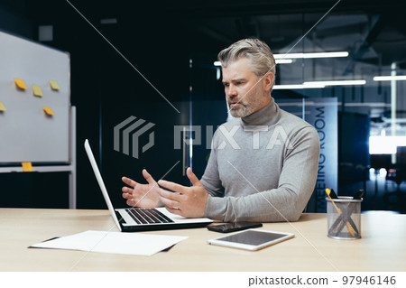 Dissatisfied gray haired boss in office, senior man disappointed with achievement result, mature businessman upset and sad working with documents and using laptop inside building. Dissatisfied gray haired boss in office, senior man disappointed with achievement result, mature businessman upset and sad working with documents and using laptop inside building. 97946146
