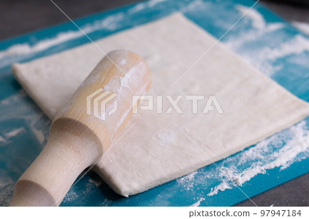 A piece of puff pastry and a wooden rolling pin on a turquoise board 97947184
