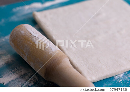 A piece of puff pastry and a wooden rolling pin on a turquoise board A piece of puff pastry and a wooden rolling pin on a turquoise board 97947186