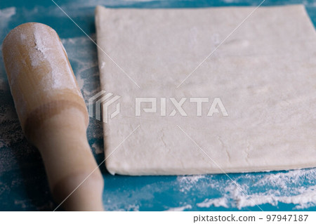 A piece of puff pastry and a wooden rolling pin on a turquoise board 97947187
