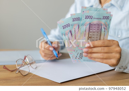 Woman holding Ukrainian 1000 bill banknotes and making notes on a blank. Count Ukrainian money Woman holding Ukrainian 1000 bill banknotes and making notes on a blank. Count Ukrainian money 97948052
