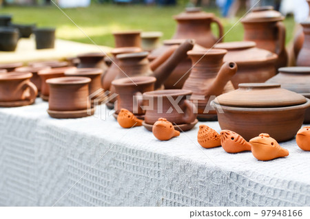 Defocus pottery from earthenware jugs mugs in nature. Set of old ceramic pot and mug, kitchen retro equipment of cooking on festival background. Ukrainian culture. Out of focus Defocus pottery from earthenware jugs mugs in nature. Set of old ceramic pot and mug, kitchen retro equipment of cooking on festival background. Ukrainian culture. Out of focus 97948166