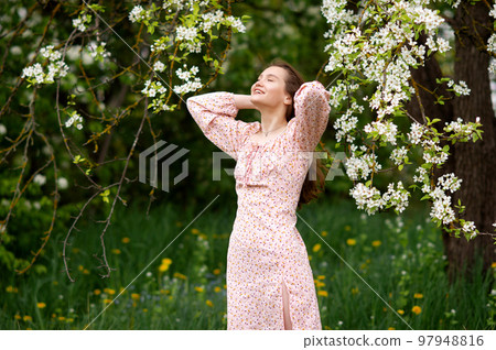 A girl in a pink dress is standing under a tree with her eyes closed and smiling A girl in a pink dress is standing under a tree with her eyes closed and smiling 97948816