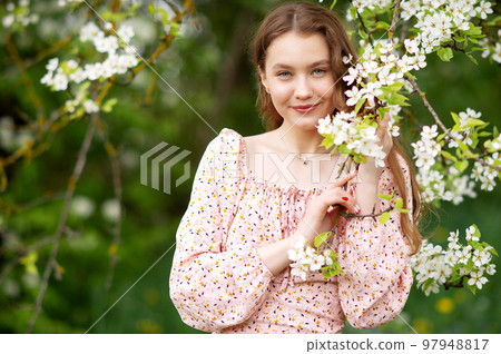 A girl in a pink dress stands near a white tree with flowers looks at the camera and smiles A girl in a pink dress stands near a white tree with flowers looks at the camera and smiles 97948817