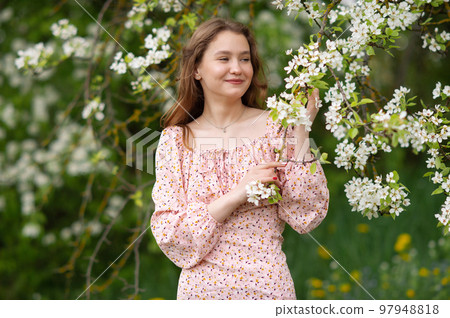 A girl in a pink dress stands near a white tree with flowers looks away and smiles A girl in a pink dress stands near a white tree with flowers looks away and smiles 97948818