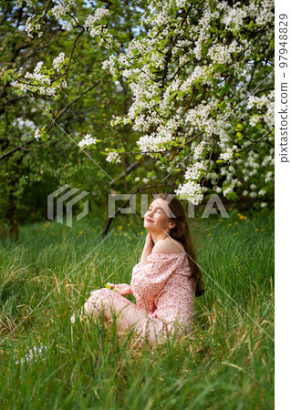 The girl is standing under a tree with her eyes closed. White petals are falling on the face The girl is standing under a tree with her eyes closed. White petals are falling on the face 97948829