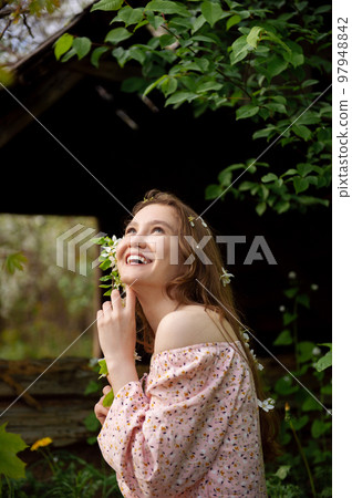 The girl is standing under a tree with her eyes closed. White petals are falling on the face The girl is standing under a tree with her eyes closed. White petals are falling on the face 97948842