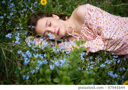 a young girl lies in the green grass with her eyes closed in a pink dress 97948844