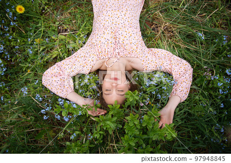 a young girl lies in the green grass with her eyes closed in a pink dress a young girl lies in the green grass with her eyes closed in a pink dress 97948845