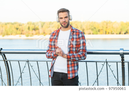 young trendy male fashion model in music headphones and casual shirt outside, modern life young trendy male fashion model in music headphones and casual shirt outside, modern life 97950061