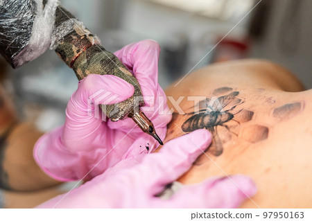 Close up of hands in pink latex gloves makes a tattoo design at client's back. Concept of International Lefthanders Day 97950163