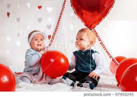 Two cute babies in fancy clothes, posing with red balloons. The concept of Valentine's day and romance 97950245