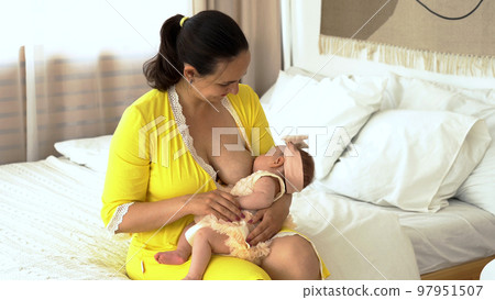 Young woman sitting on the bed and feeding her baby with breast 97951507