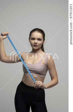 Happy slim brunette woman in sport wear with measuring tape on white background. Positive weight loss diet results. Healthy lifestyles concept. Happy slim brunette woman in sport wear with measuring tape on white background. Positive weight loss diet results. Healthy lifestyles concept. 97951951