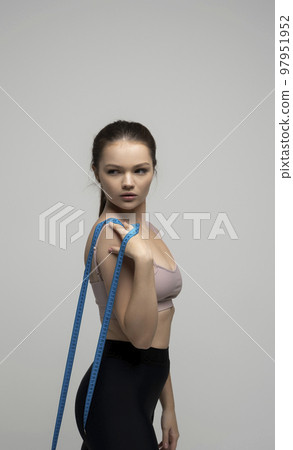 Woman with a perfect shape of healhy body standing with measuremt tape and happy with result of exercise training on white studio background. Weight loss and healthy lifestyles concept. Woman with a perfect shape of healhy body standing with measuremt tape and happy with result of exercise training on white studio background. Weight loss and healthy lifestyles concept. 97951952