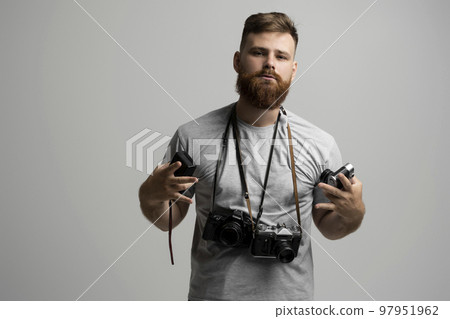 Portrait of bearded photographer with a bunch of different vintage old film cameras. Close up portrait of man holding vintage camera. Film photography. 97951962