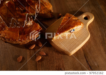 King cake or galette des rois in French. Epiphany pie with golden paper crown and little ceramic figurine King cake or galette des rois in French. Epiphany pie with golden paper crown and little ceramic figurine 97952162