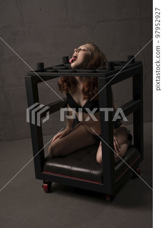 Provocative female showing tongue sitting in bondage cage 97952927