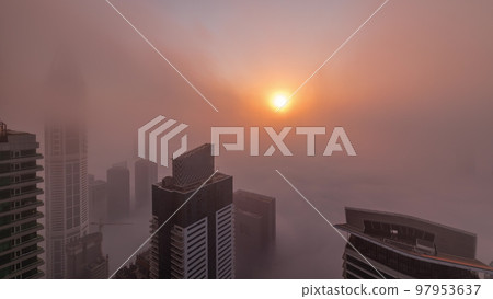 Rare early morning winter fog above the Dubai Marina skyline and skyscrapers lighted by sun aerial timelapse. 97953637