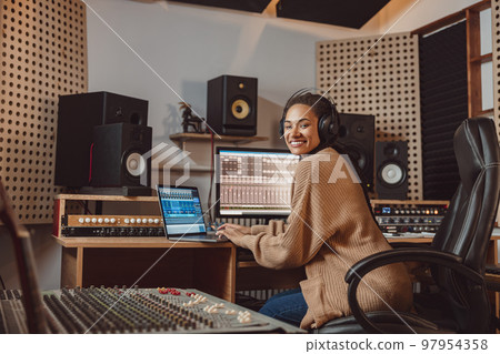 Cheerful multiracial anchor woman, presenter, sound engineer, musician, producer working in a professional music studio 97954358