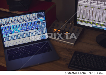 Close-up switched on laptop and monitor screen with mixing panel on a table in a broadcasting and sound recording studio 97954362